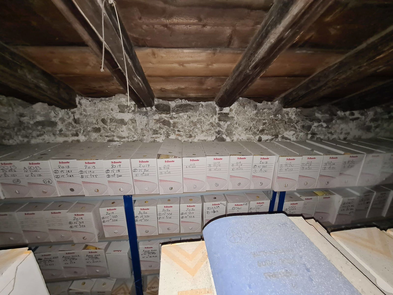 Boîtes d'archives empilées dans un grenier en pierre.