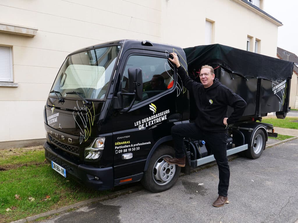 Homme souriant à côté d'un camion de débarras.
