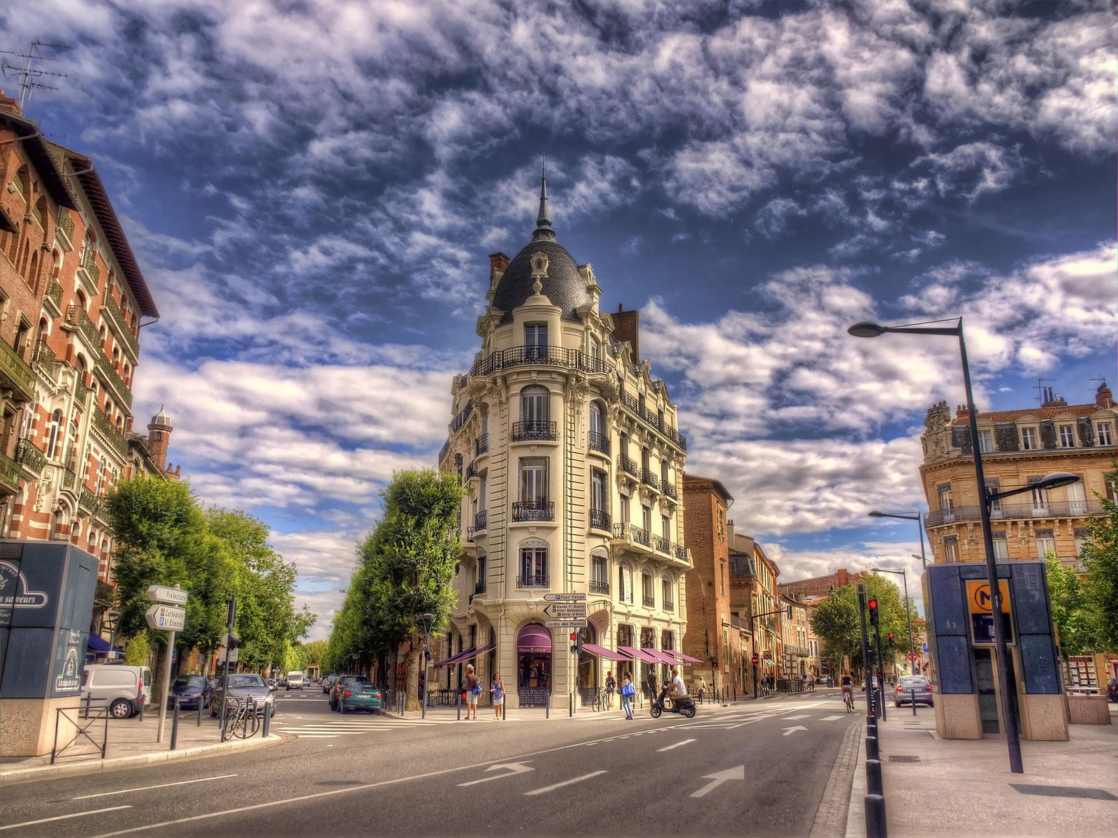 Avenue bordée d'immeubles anciens et de nuages.