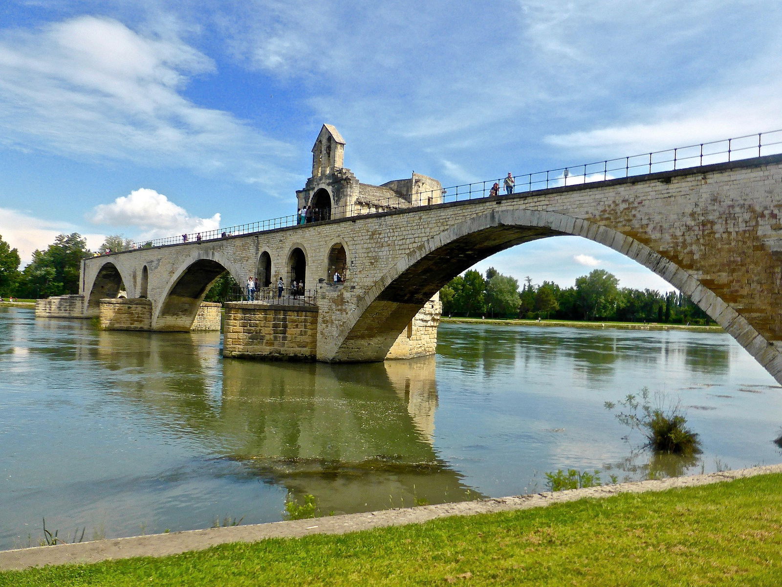 Pont médiéval sur rivière sous ciel bleu.