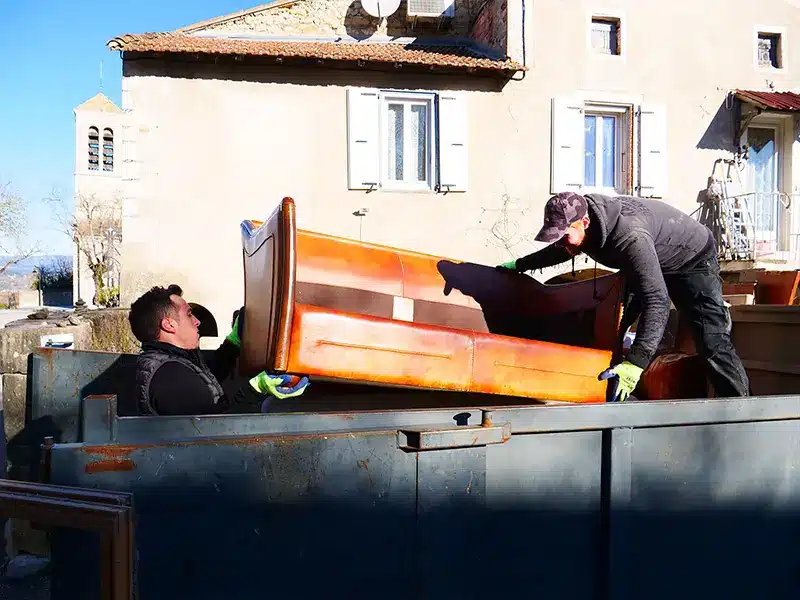 Deux hommes chargent un canapé dans une benne.